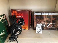 Photo showing the VHS set boxed and lined together, AKG K240 headphones on a stand with their original Sextett Cardan packaging, and a box of Scotch 142 magnetic tape.