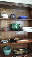 Shelf displaying two ceramic teapots, various bowls and planters, antique Dutch plate, and trays.