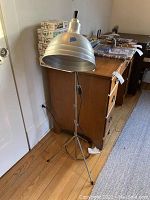 Full view of vintage Acme-Lite lamp showing adjustable aluminum shade on tripod base near wooden dresser and model kits.