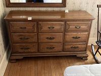 Front view of solid oak dresser showing nine drawers and decorative drawer fronts with brass-tone handles.