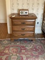First solid oak vintage end table showing three drawers with decorative metal handles and bracket feet under a wooden top, all finished in medium oak tone.