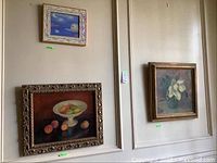 All three paintings hung on wall: top left a cosmic scene with bird, bottom left a fruit still life, right a floral still life