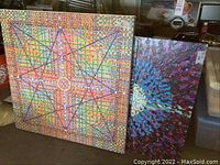 Two original acrylic paintings by Wilfred Sarr displayed side by side, one with colorful abstract star pattern and one with circular floral pattern