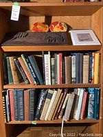 Overview of top shelf showing carved panel, oval plaques, art prints and books below
