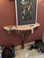 Front view of ornate wooden side table with white marble top mounted on wall, decorative carvings and single front leg visible.