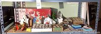 Wide shot of shelf with red “Holiday Greetings” greeting card box in back, white ceramic ghost, assorted small items and ornament boxes on table