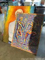 Two original paintings by Wilfred Sarr leaning against furniture, clearly showing abstract and figurative compositions.