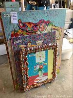 Group of three paintings stacked: front canvas piece with foam frame, two Masonite paintings behind.