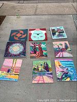 Overhead shot of nine acrylic-on-masonite paintings laid on concrete