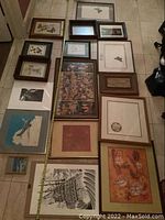 Full layout overhead image displaying 16 framed art prints on a tiled floor. The prints depict a variety of subjects including fruit, animals, classic figures, and a sailing ship. Frames vary in color and style.