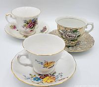 Photo showing three antique bone china teacups with matching saucers, highlighting the different floral patterns and gold gilt detailing on rims and handles.