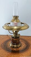 Front view of antique gas lamp converted to electric showing brass top ring, frosted glass reservoir, wood base, and clear chimney.