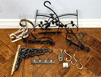 Photo displaying a variety of metal shelf brackets, plant hangers with leaf motifs, and assorted hooks arranged on wooden floor.