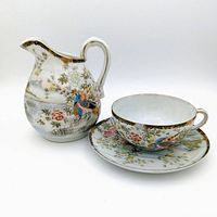 Teacup, saucer, and creamer jug shown together with detailed nature-themed design and gold trim.