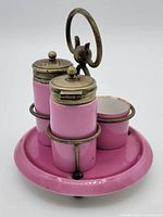 Side view of two pink ceramic shakers with tarnished metal lids in a matching pink tray with rusted metal holder