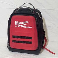 Front view of Milwaukee Packout backpack showing red front panel with logo, black trim and straps.