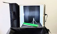 Image showing the portable photo studio tent set up with green backdrop roll and mini tripod inside, lit by built-in lighting panels