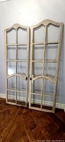 Pair of tall antique wooden doors with multiple glass panels, standing side by side against a wall, showing overall design and condition.