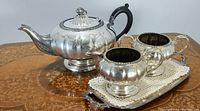 Photo showing the full tea set - teapot, creamer, sugar bowl on separate oval tray on a wooden table