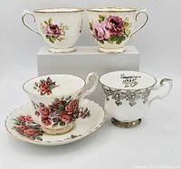 Photo of four Royal Albert bone china tea cups featuring rose patterns and commemorative design, one with matching saucer.
