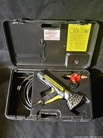 Opened hard black plastic case showing metal commercial heat tool with attached hose and red propane regulator inside molded slots.