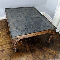 Full view of square coffee table with glass top over antique door base showing carved panels.
