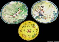 Three vintage artistic plates featuring Asian motifs laid out flat on a black background: two with women in traditional dress and one yellow with floral patterns.