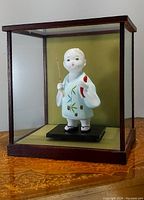 Full view of the porcelain doll inside the glass case showing its size and wood framed glass display.