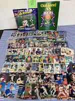 Multiple baseball cards, an Oakland A's 1976 yearbook, and an action figure displayed on a flat surface