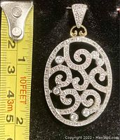 Close-up of pendant beside measuring tape showing length of about 2 inches