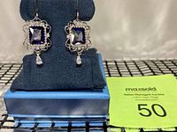 Front view of the pair of earrings displayed on a blue stand with original blue gift box beneath.