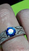 Close-up image showing detailed milgrain beaded design on silver band and vibrant royal blue simulated tanzanite center stone held by prongs.