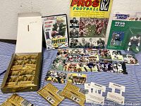 Wide view of the collectors lot showing unopened Pinnacle football card packs in gold box, opened football cards laid out, a 1962 Pros Football magazine, a 1996 Starting Lineup football action figure packaged, and a football DVD.