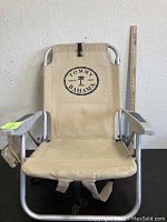 Full view of the beige Tommy Bahama beach chair showing aluminum frame, beige fabric, armrests, and backpack straps for carrying.
