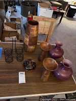 Photo showing entire lot on table including purple glass vases, wooden candle holders, ceramic candle holder, wire holders, and wooden container.