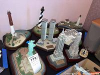Overview photo showing multiple Danbury Mint statues including Twin Towers, Empire State Building, lighthouses, and Statue of Liberty on table