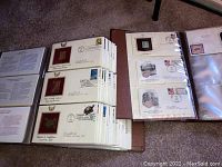 Photo showing multiple album pages with first day cancellation stamps featuring metallic designs and dated postmarks from 2003, 2004, and 2006.