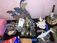 Top-down wide shot showing four blue resin dolphin sculptures, white fine china dolphin sculpture, and clear crystal dolphin sculpture, alongside other decor.