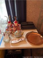 Photo showing oil and vinegar bottles, a floral teapot-shaped cookie jar, spoon rest, and small glass vase on table with servimg items.