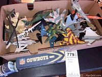 Photo of about 15 metal toy airplanes with various military designs in a cardboard box, with a die cast Dallas Cowboys truck on a shelf below.