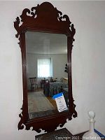 Front view of large mahogany wall mirror with carved detailing showing full frame and mirror surface reflecting a window and room.