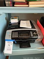 Brother MFC-490CW all-in-one printer, front view showing control panel with buttons and LCD screen, with tracking tag attached.