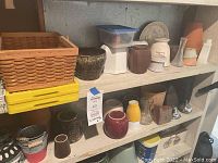 Wide view of ceramic pots and vases alongside woven baskets and plastic crates on shelves.