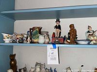 Shelf containing multiple ceramic and china decorative items including pitchers, animal figurines, human figurines