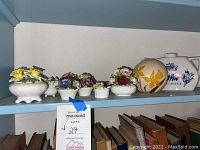 Full view of the hand painted floral bone china pieces with two ceramic liquor bottles on a shelf.