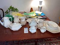 Full lot showing white Ironstone china collection including teapot, pitchers, covered serving dish, condiment containers and large platter on wooden table.
