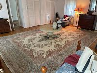Large ivory wool area rug with central dark floral medallion and red-green floral border, cotton fringe visible at edges.