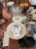Overview of clear glass salad bowls, white embossed dinner plates, and assorted tableware on a wooden table.