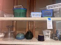Shelf containing small vases and ceramic pots along with plastic storage baskets above
