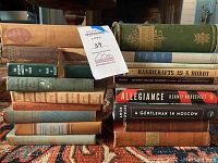 Vintage hardcover books stacked and arranged showing spine titles and varying covers with a note tag.